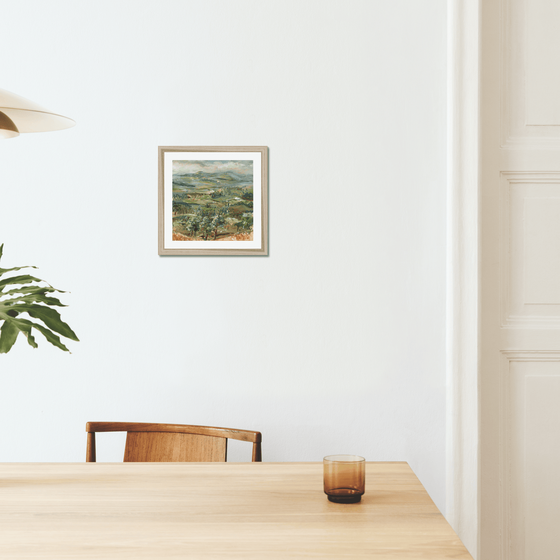 landscape by artist rebecca carr on the wall in a dining room setting with plants