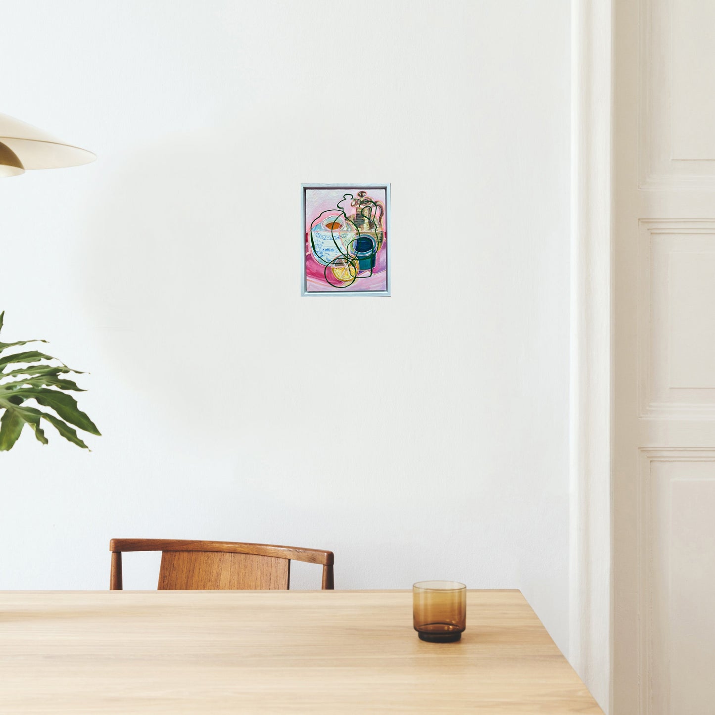 Colourful still life painting by rebecca carr on a white wall above a wooden table with a glass.