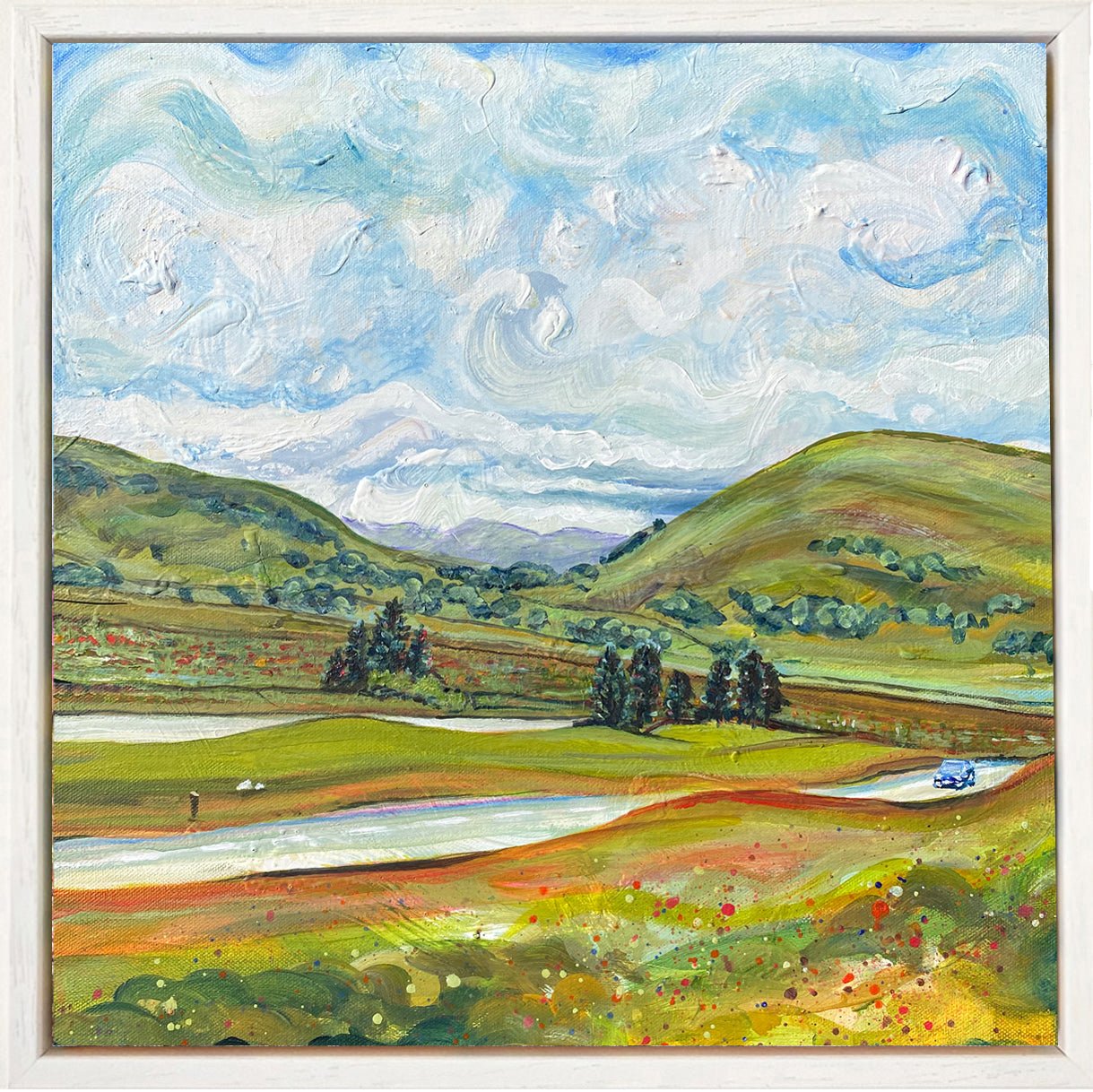 Framed painting of view from Windy Fell with distant peaks, expressive sky, and small blue car on countryside road.
